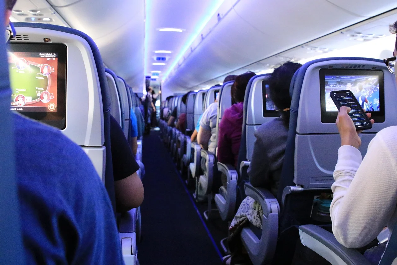 Wnętrze samolotu, pasażerowie przy ekranach i telefonie podczas odprawy online Ryanair