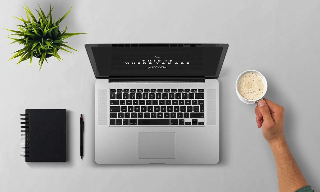 Laptop do planowania podróży, filiżanka kawy i notatnik na biurku, jak tanio kupić bilety lotnicze